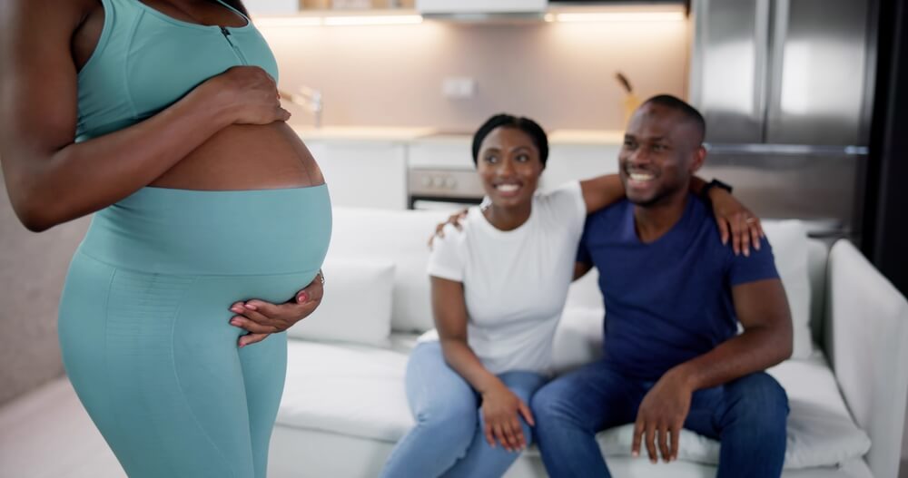 A smiling couple with their pregnant surrogate